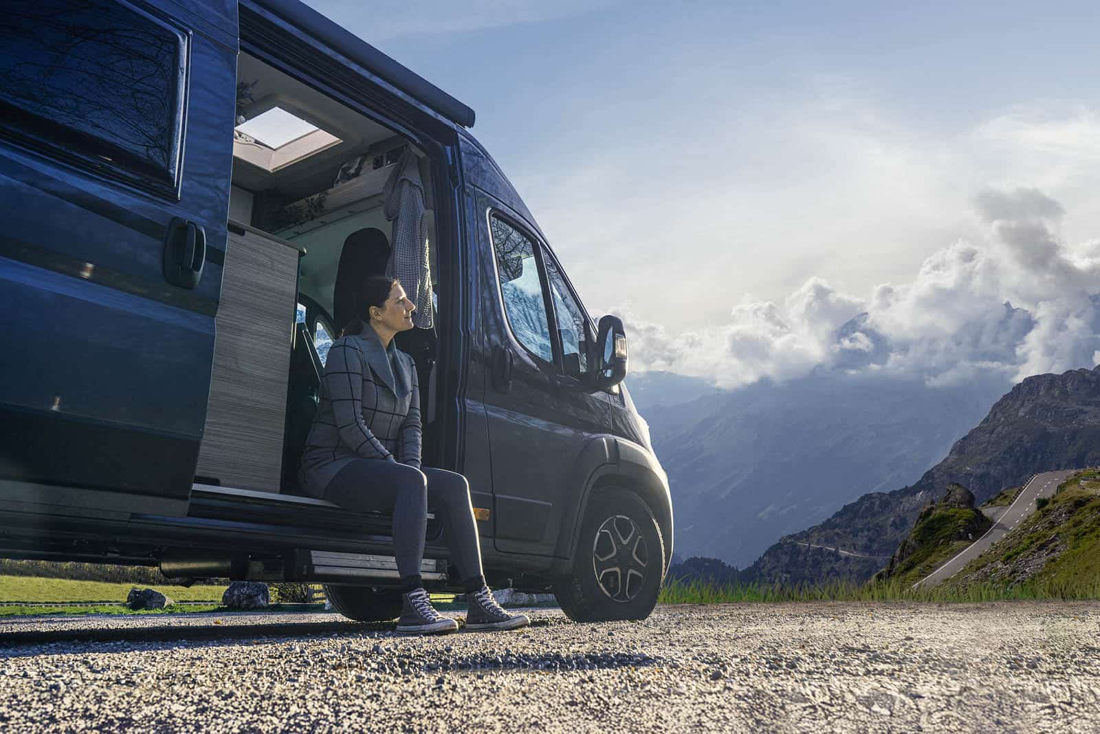 Die Frau sitzt im Wohnmobil und schaut sehr melancholisch in Richtung Berge.