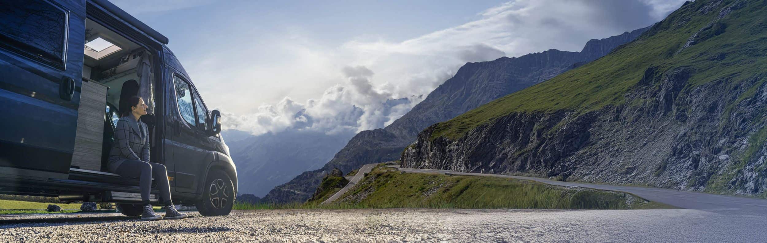Die Frau sitzt im Wohnmobil und schaut sehr melancholisch in Richtung Berge.