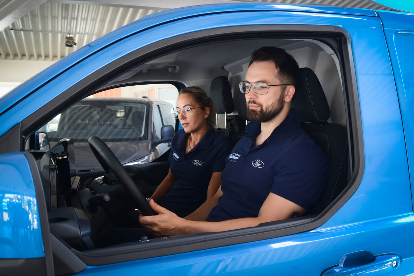 Zwei Mitarbeiter sitzen in einem blauen Fahrzeug.