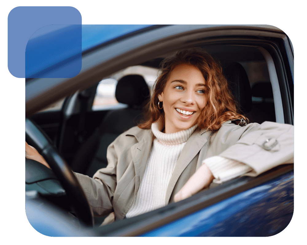 Eine Frau sitzt am Steuer eines blauen Wagens und lächelt zum Fenster.
